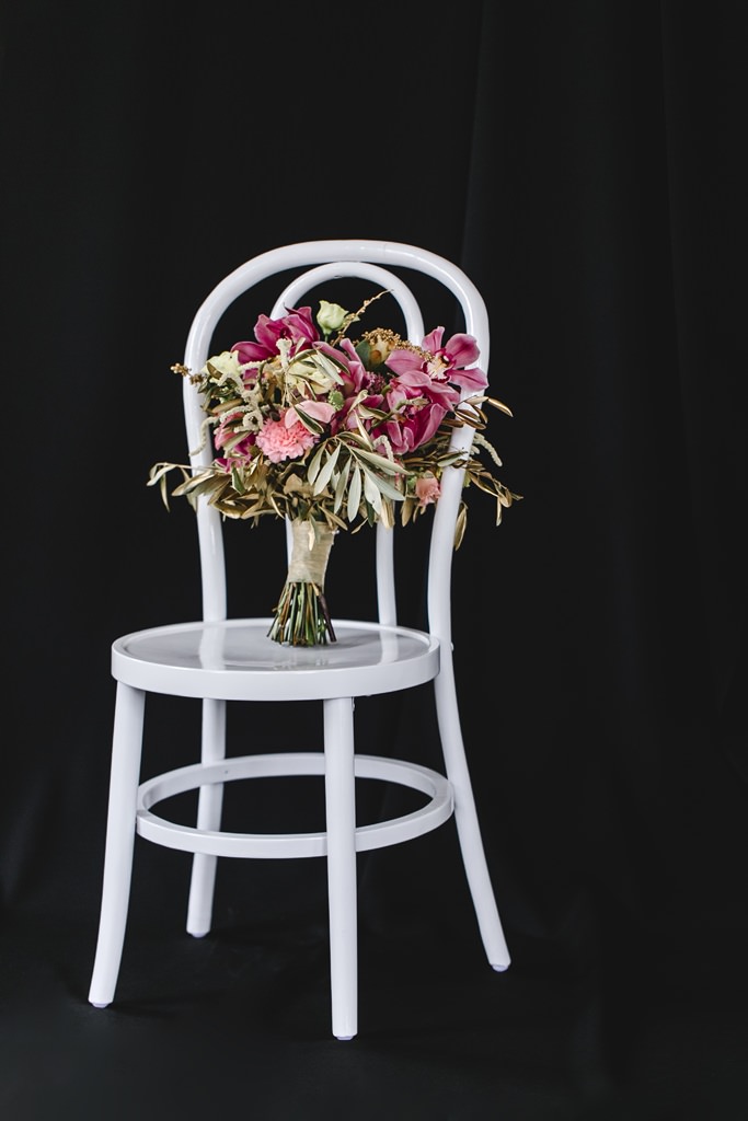 besondere Brautstraussidee in rosa und gold, präsentiert auf einem weißen Stuhl