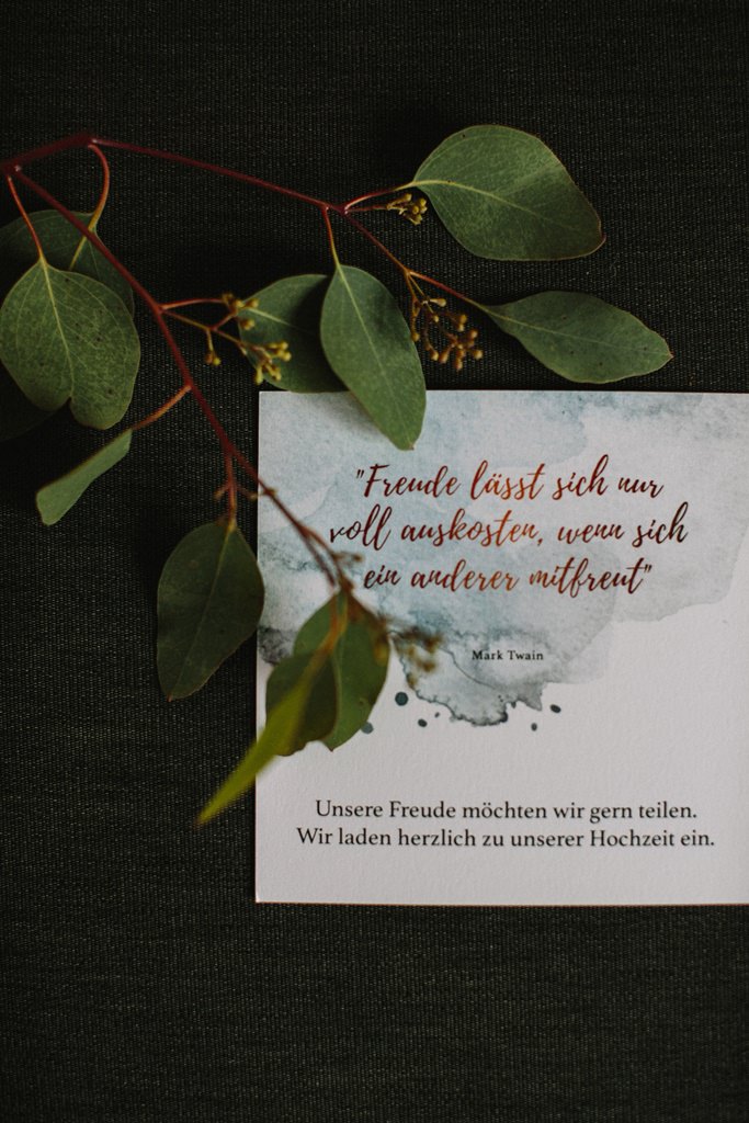 Hochzeitsfotoidee: Die Einladungskarte wird mit einem Zweig fotografiert