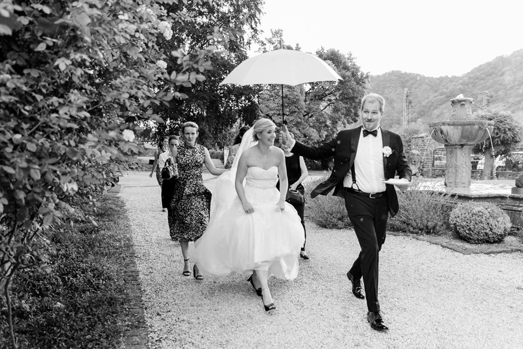 Hochzeitsfoto Idee bei Regen: Der Bräutigam hält einen Regenschirm über die Braut