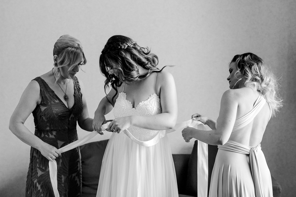 Mutter und Freundin helfen der Braut ihr Brautkleid anzuziehen