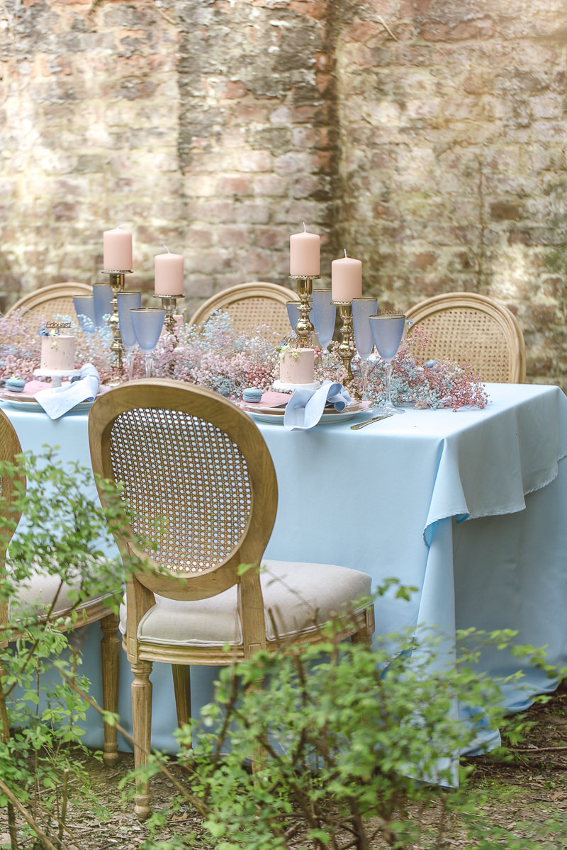 Tischdeko mit hellblauer Tischdecke, blauen Gläsern, rosafarbenen Kerzen und Blumen in Rosa- und Blautönen