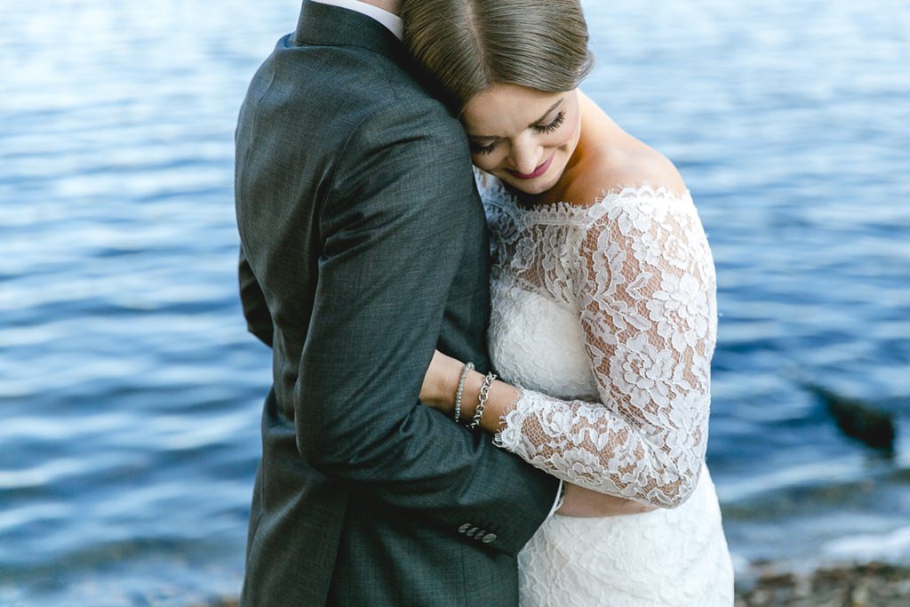 eine Braut in einem Brautkleid mit Spitze und langen Ärmeln schmiegt sich an den Bräutigam | Foto: Hanna Witte