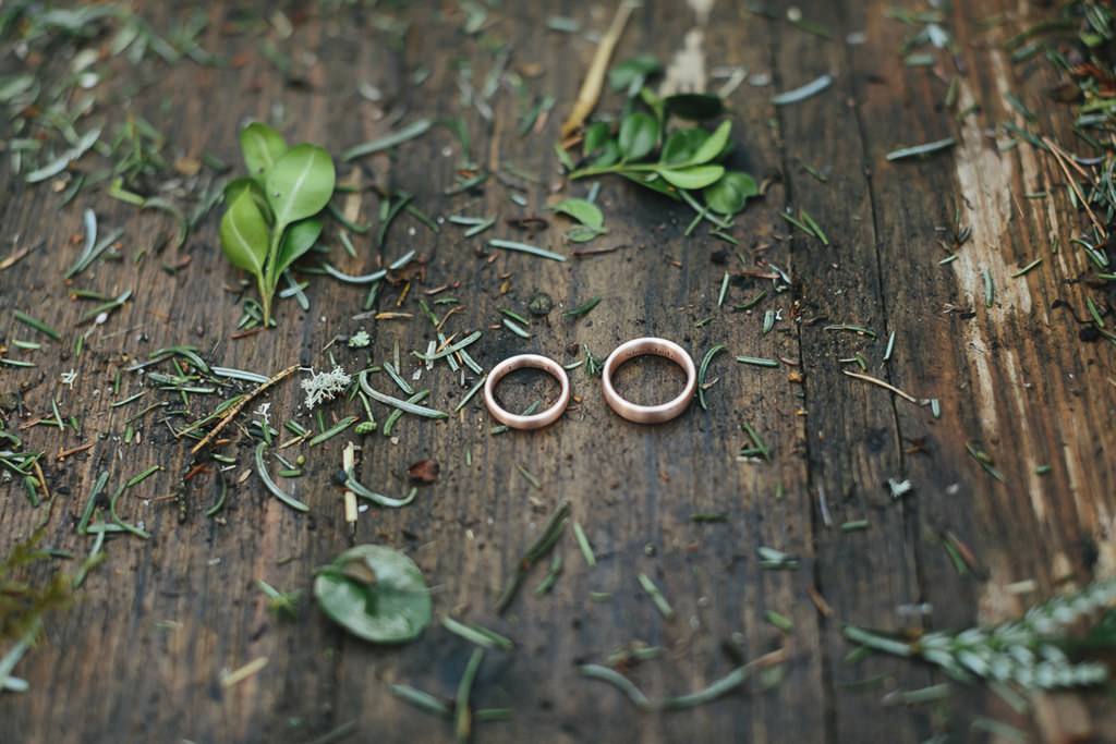 Hochzeitsfotoidee Trauringe: Die Eheringe liegen neben Tannennadeln auf einem nassen Holzboden | Foto: Hanna Witte
