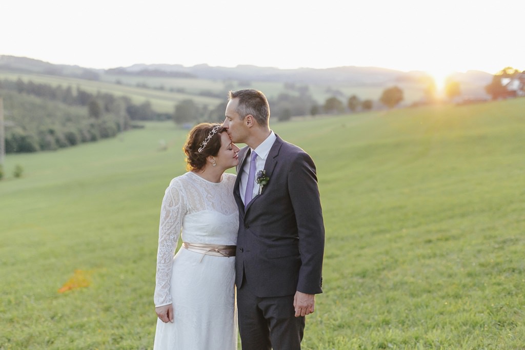 Paarshooting in der Natur: Braut und Bräutigam stehen bei Sonnenuntergang Arm in Arm auf einer Wiese im Sauerland | Foto von Hochzeitsfotografin Hanna Witte