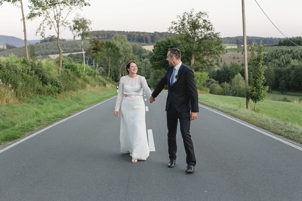 während des Paarshootings laufen Braut und Bräutigam über eine ruhige Straße im Sauerland