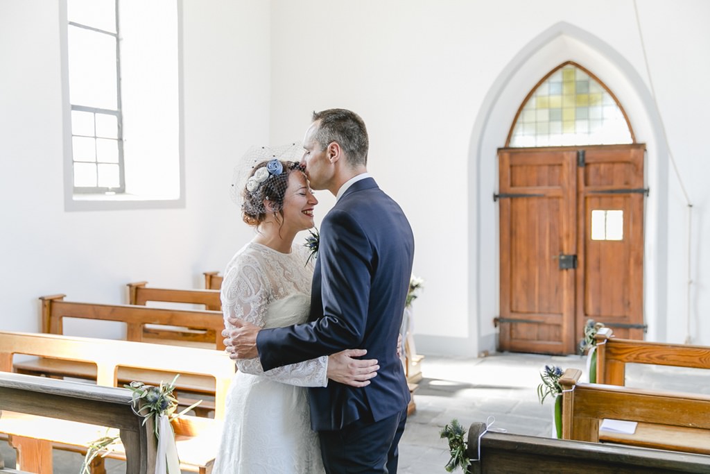 Paarshooting in einer kleinen Kapelle: Der Bräutigam küsst die Braut liebevoll auf die Stirn | Foto von Hochzeitsfotografin Hanna Witte