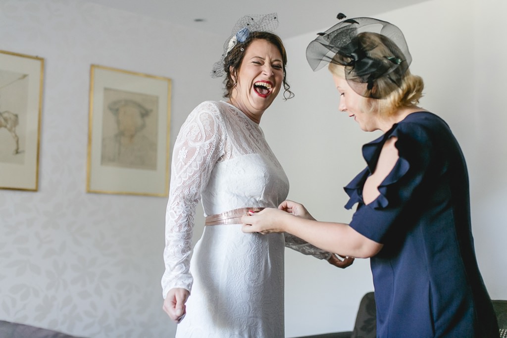 eine Freundin richtet das Band über dem Brautkleid der Braut | Foto von Hochzeitsfotografin Hanna Witte