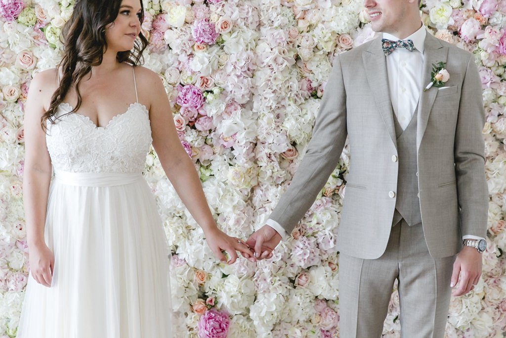das Brautpaar steht Hand in Hand vor einer wunderschönen Flower Wall | Foto: Hanna Witte
