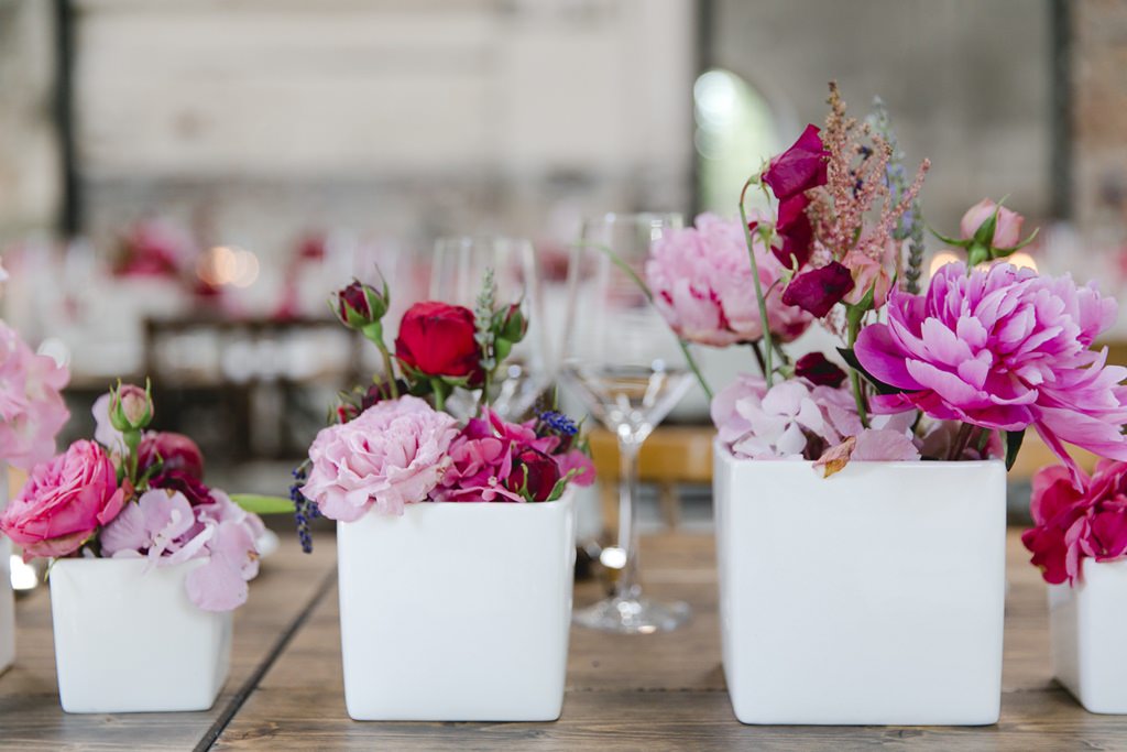 viereckige, weiße Blumenvasen mit Hochzeitsblumen in Rosa, Pink und Rot als Tischdeko | Foto: Hanna Witte