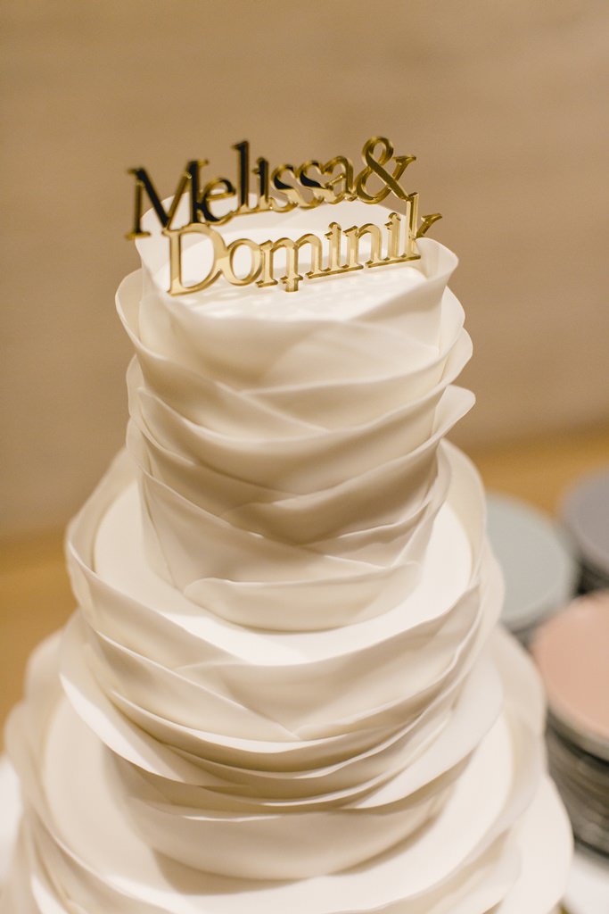 weiße, gefächerte Hochzeitstorte mit goldenem Cake Topper | Foto: Hanna Witte