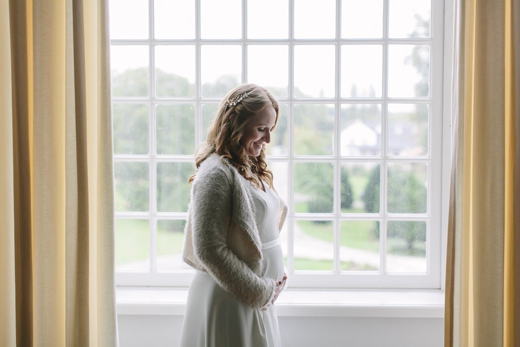 Hochzeitsfoto einer schwangeren Braut, die vor einem hohen Fenster steht | Foto: Hanna Witte