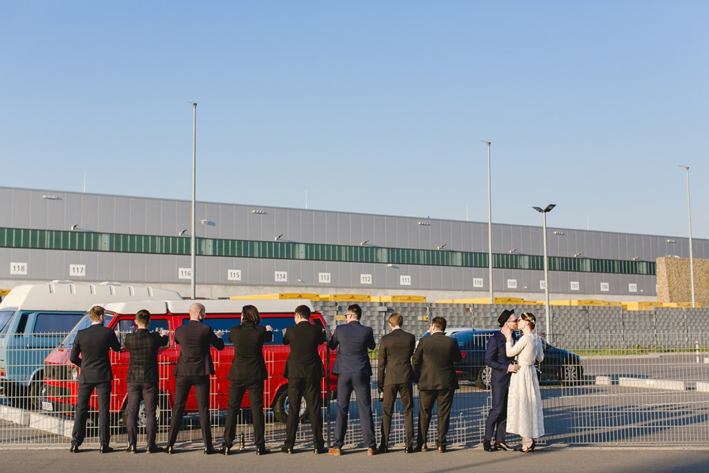 Gruppenfotoidee Hochzeit: Das Brautpaar steht neben einer Reihe von Freunden, die der Kamera den Rücken zukehren | Foto: Hanna Witte