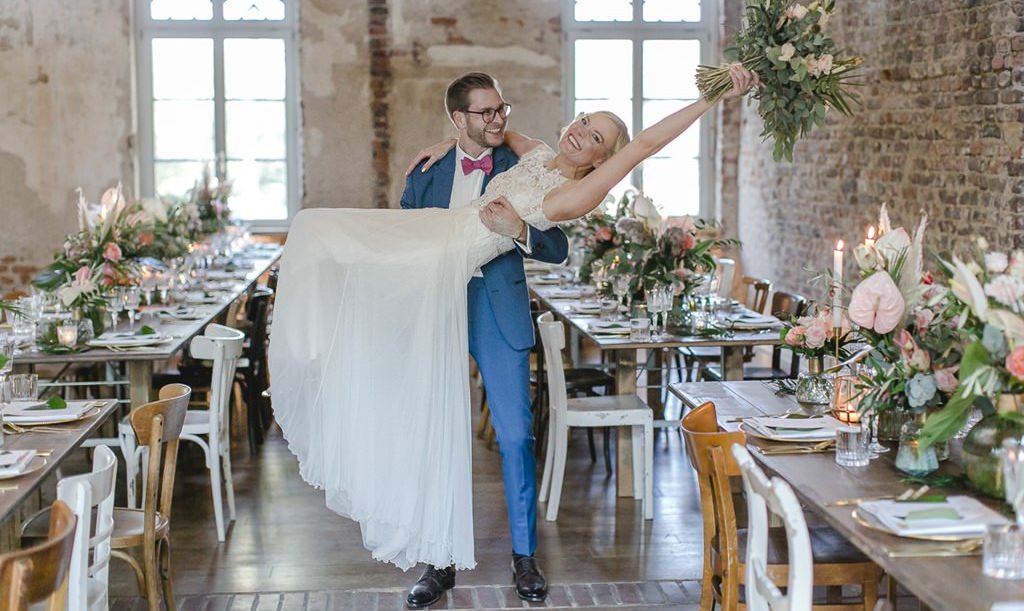 der Bräutigam trägt die Braut im Festsaal von Rittergut Orr auf Händen | Hochzeitsfoto: Hanna Witte