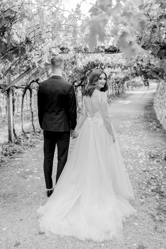 Braut und Bräutigam gehen einen Feldweg zwischen Weinreben entlang | Bild: Hochzeitsfotografin Hanna Witte