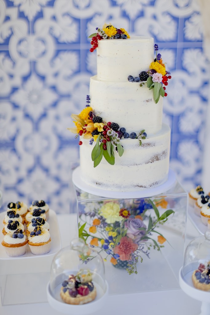 weiße Undone Hochzeitstorte mit einer Deko aus blauen Beeren und bunten Sommerblumen | Foto: Hanna Witte