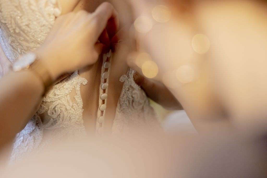 die Trauzeugin schließt die Knopfleiste des Brautkleids | Foto: Hanna Witte