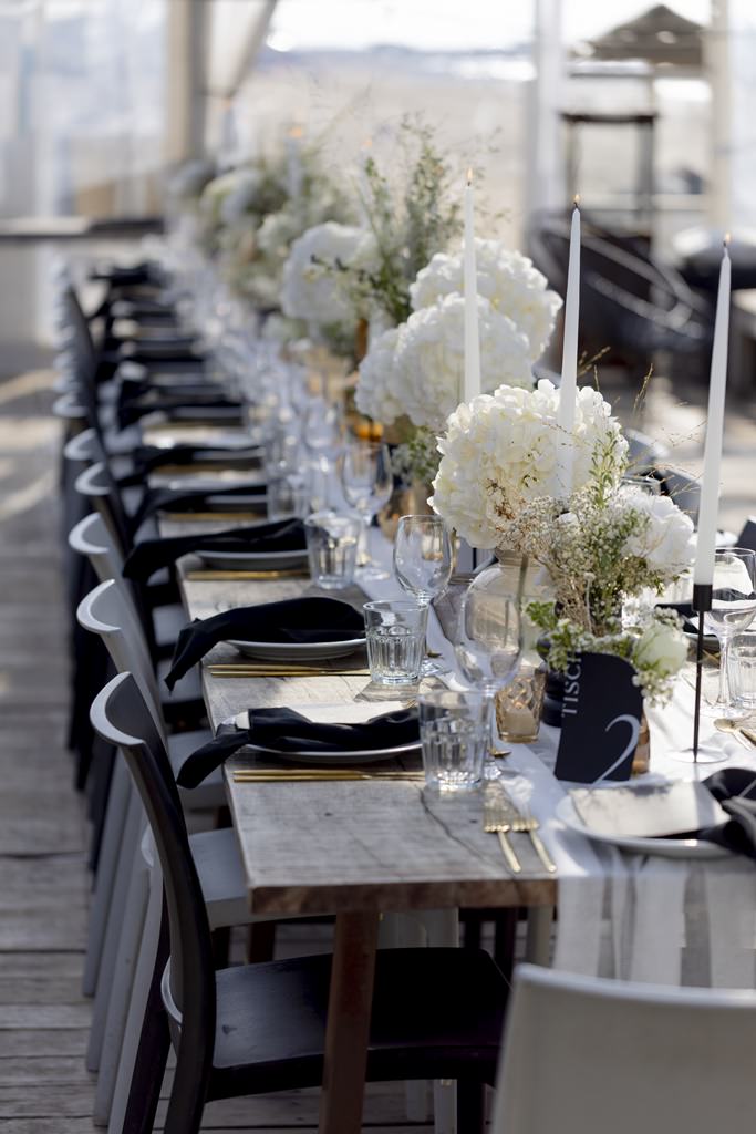 Hochzeitstischdeko in schwarz, gold und weiß mit Hortensienblüten, schwarzen Stühlen und rustikalen Holztischen | Foto: Hanna Witte