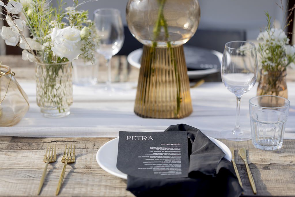 Hochzeitsgedeck mit goldenem Besteck, schwarzer Menükarte, weißem Teller und schwarzer Stoffserviette | Foto: Hanna Witte