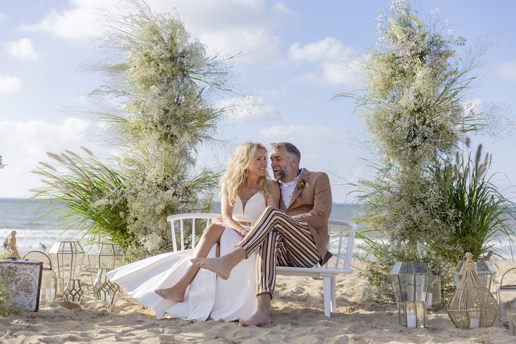 das Ehepaar sitzt während der Erneuerung des Eheversprechens auf einer Bank am Strand, umgeben von Blumendeko und Laternen | Foto: Hanna Witte