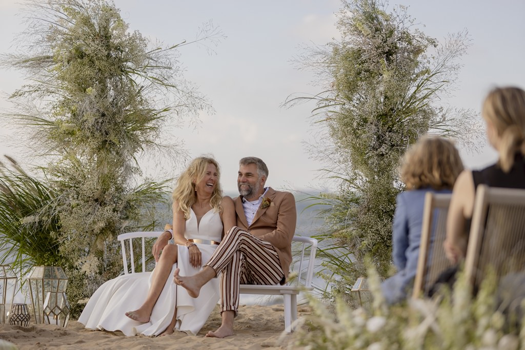 das Brautpaar sitzt während der Erneuerung des Eheversprechens auf einer weißen Traubank am Strand | Foto: Hanna Witte
