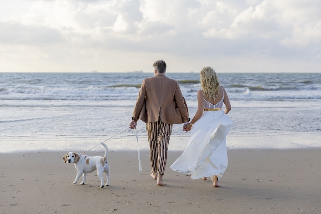 das Brautpaar geht Hand in Hand mit dem Hund an der Leine am Strand spazieren | Foto: Hanna Witte