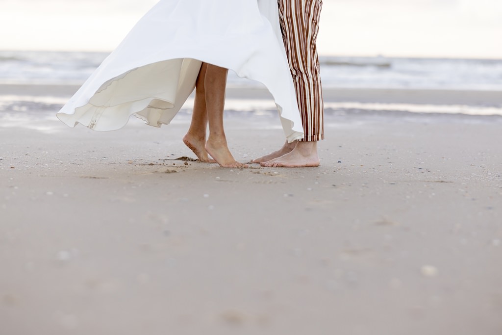 die Beine und nackten Füße des Brautpaares im Sand mit den Wellen im Hintergrund | Foto: Hanna Witte