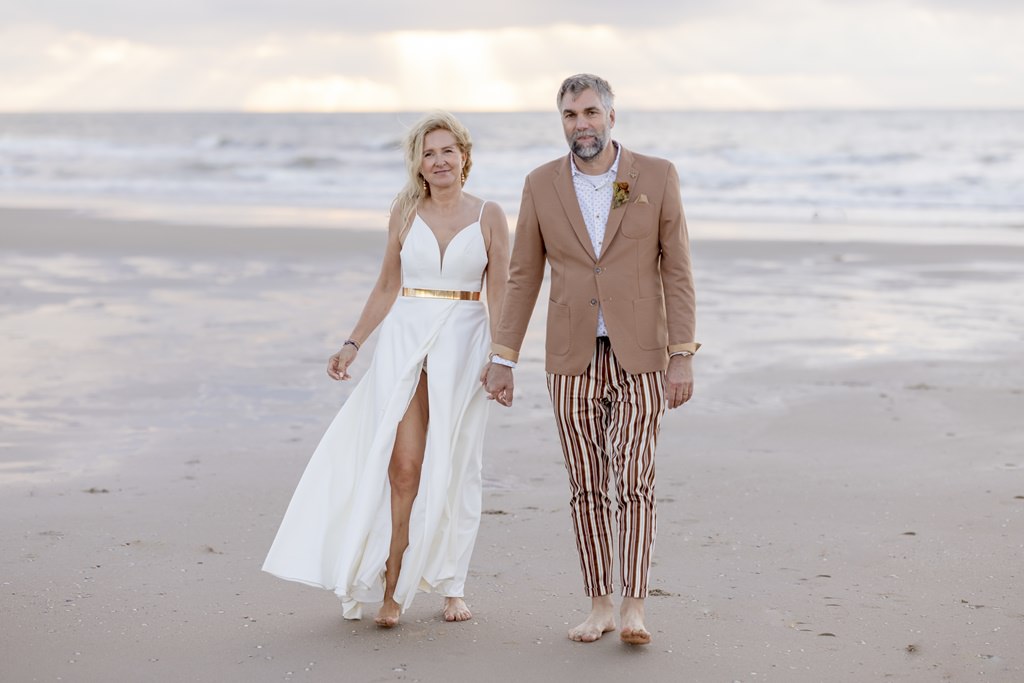 das Brautpaar läuft am Strand Hand in Hand vom Meer weg und auf die Kamera zu | Foto: Hanna Witte