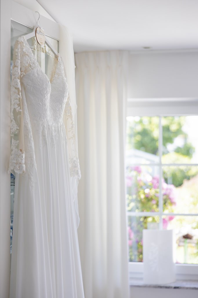 vor dem Getting Ready hängt das Brautkleid mit einem Kleiderbügel an der Tür | Hochzeitsfoto: Hanna Witte