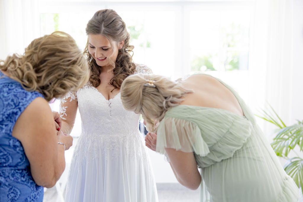 Mutter und Trauzeugin richten die langen Ärmel des Brautkleides | Hochzeitsfoto: Hanna Witte