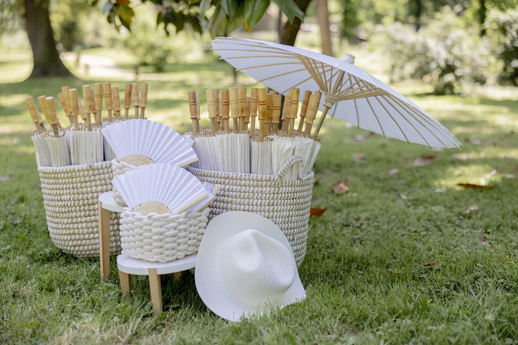 weiße Papier Sonnenschirme und Fächer stehen in geflochtenen Körben für die Hochzeitsgäste bereit | Hochzeitsfoto: Hanna Witte