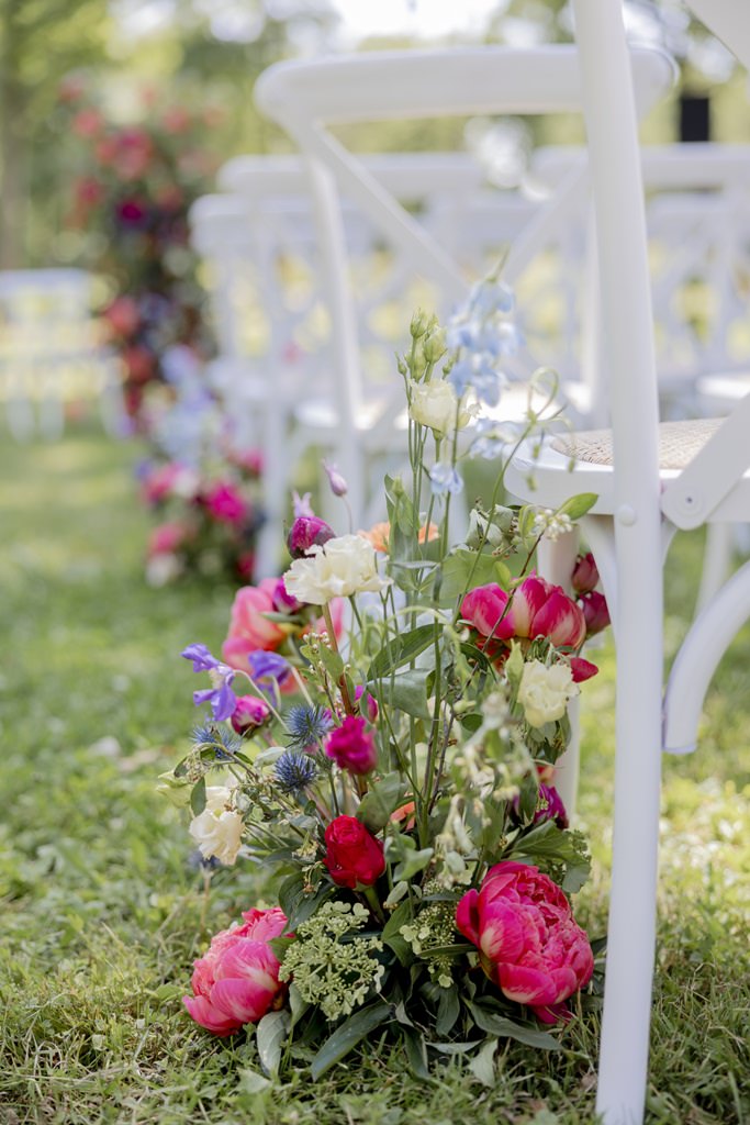 Blumendeko in pink, blau und grün für den Gang einer Trauung im Freien | Hochzeitsfoto: Hanna Witte