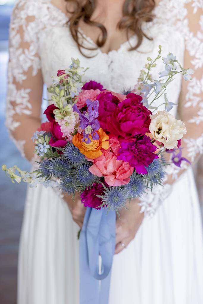 die Braut hält ihren Brautstrauß in pink, blau, orange und lila in den Händen | Hochzeitsfoto: Hanna Witte