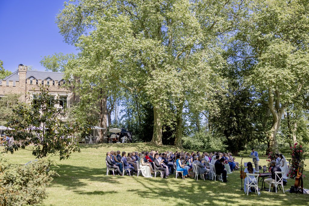 die Hochzeitsgesellschaft während der Freien Trauung unter hohen Bäumen auf der Wiese von Rittergut Orr | Hochzeitsfoto: Hanna Witte