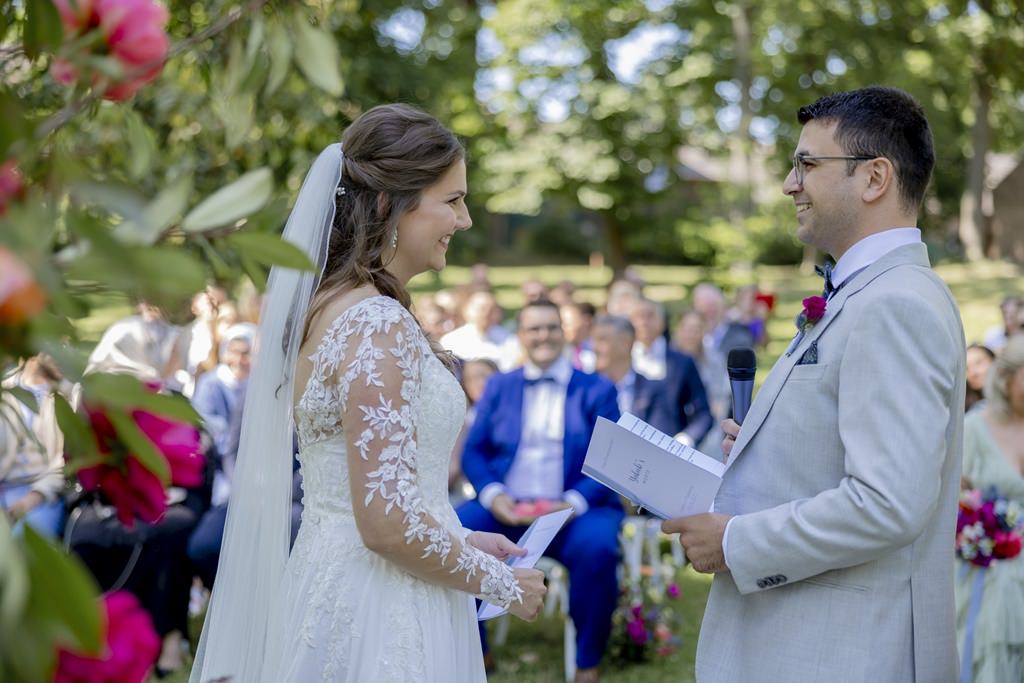 das Brautpaar steht vor den Hochzeitsgästen und hält sein Eheversprechen in den Händen | Hochzeitsfoto: Hanna Witte