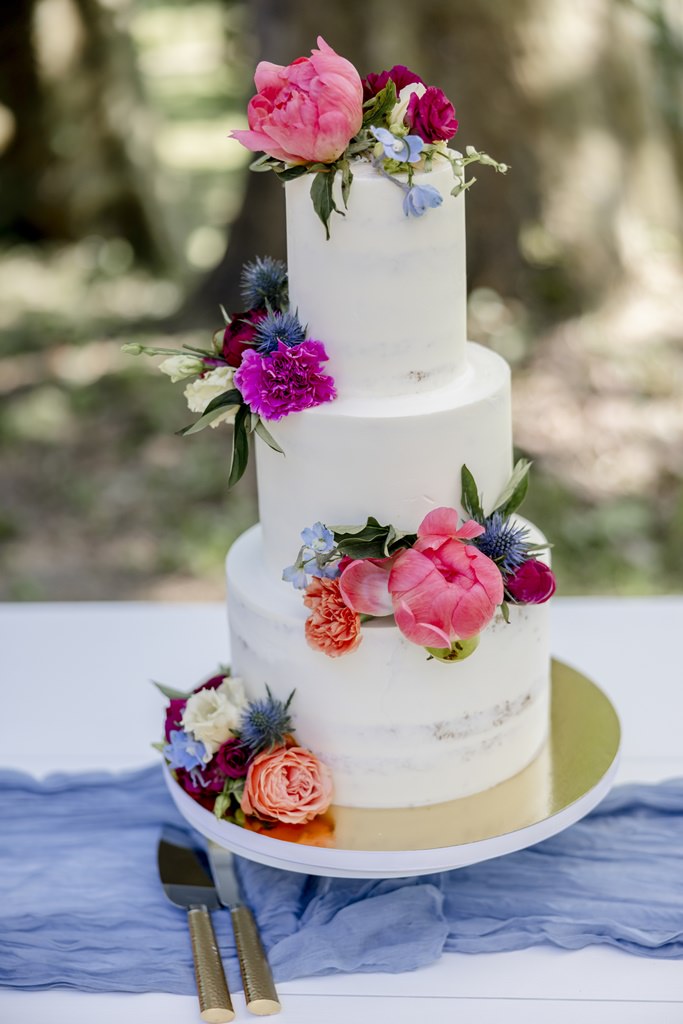 dreistöckige half naked cake Hochzeitstorte mit Blumendeko in pink, rosa, orange und blau | Hochzeitsfoto: Hanna Witte