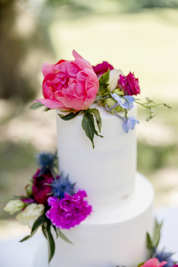 weiße Hochzeitstorte mit bunter Blumendeko in pink, rosa und blau | Hochzeitsfoto: Hanna Witte