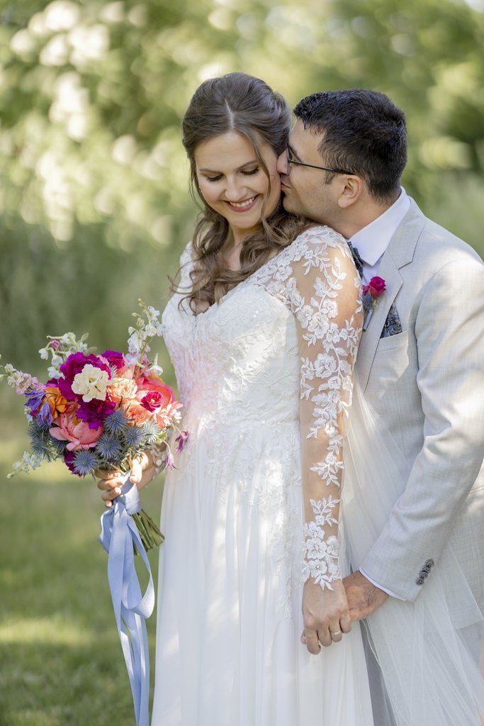 der Bräutigam küsst die Braut zärtlich auf die Wange, während er hinter ihr steht | Hochzeitsfoto: Hanna Witte