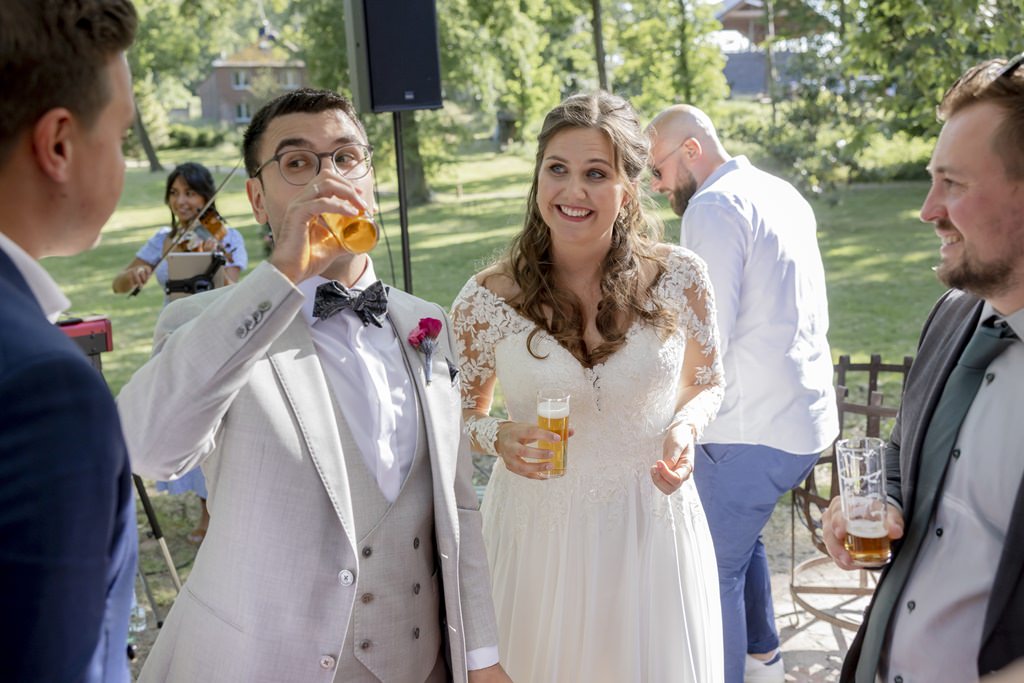 das Brautpaar einer Hochzeit im Rittergut Orr trinkt beim Sektempfang ein Kölsch mit den Gästen | Hochzeitsfoto: Hanna Witte