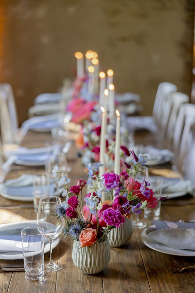 langer Hochzeitstisch mit vielen kleinen Blumenarrangements in knalligen Farben und schmalen Kerzen | Hochzeitsfoto: Hanna Witte