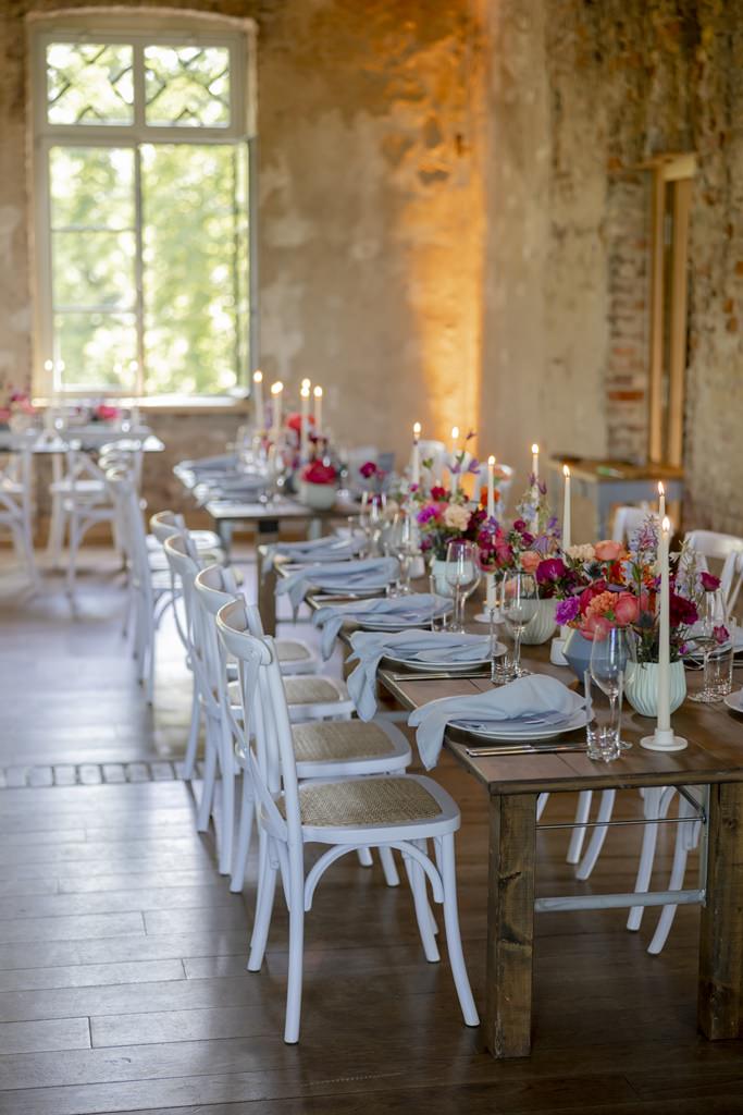 rustikale lange Hochzeitstische mit Crossback Chairs, bunter Blumendeko und schmalen Kerzen | Hochzeitsfoto: Hanna Witte