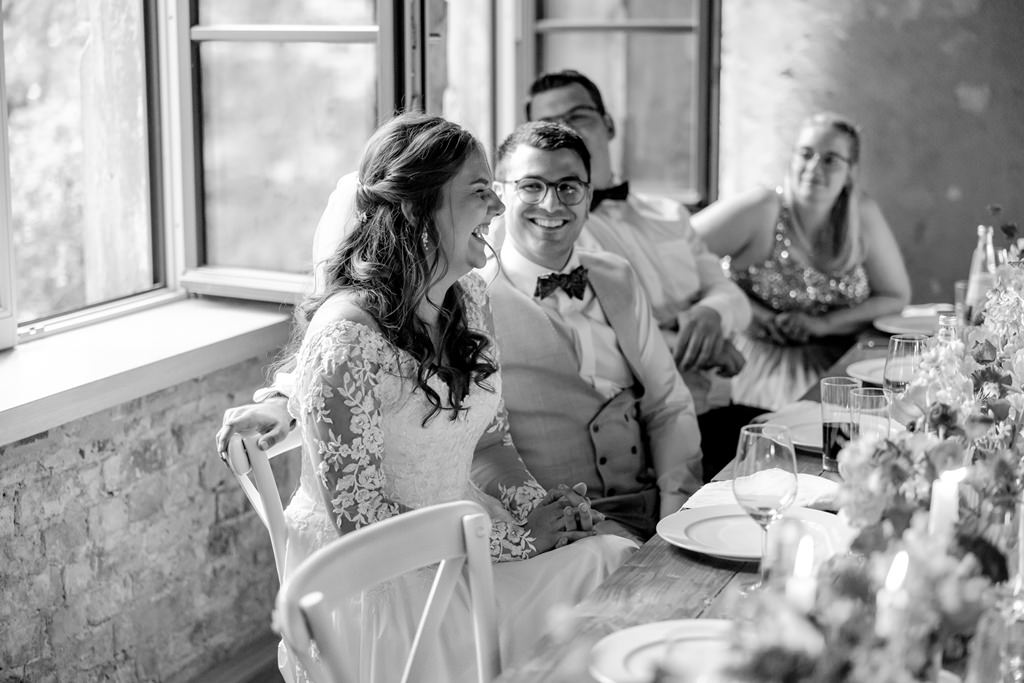das Brautpaar lacht während einer Rede bei der Hochzeitsfeier | Hochzeitsfoto: Hanna Witte
