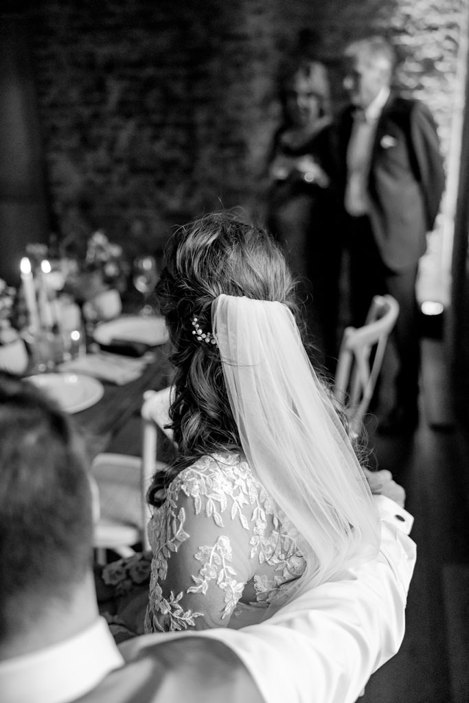 Braut und Bräutigam sitzen an der langen Hochzeitstafel | Hochzeitsfoto: Hanna Witte