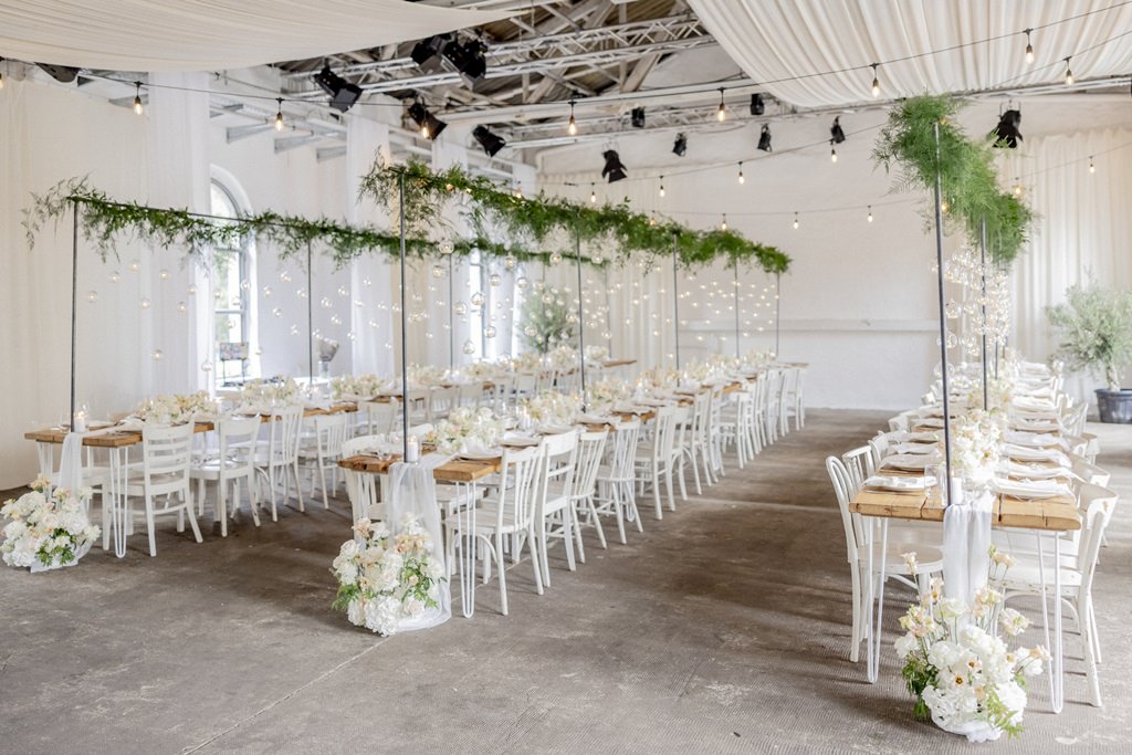drei lange Hochzeitstische mit weißen Stühlen und Hängedeko aus Greenery und Kerzen in Glaskugeln | Foto: Hanna Witte