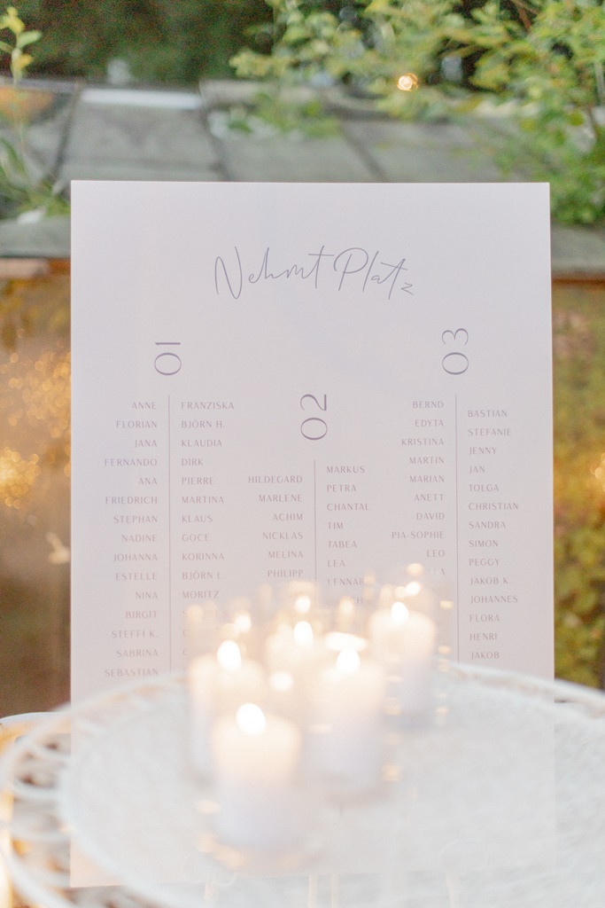 weißer Hochzeits-Sitzplan mit feiner, grauer Schrift, davor leuchten Kerzen | Foto: Hanna Witte