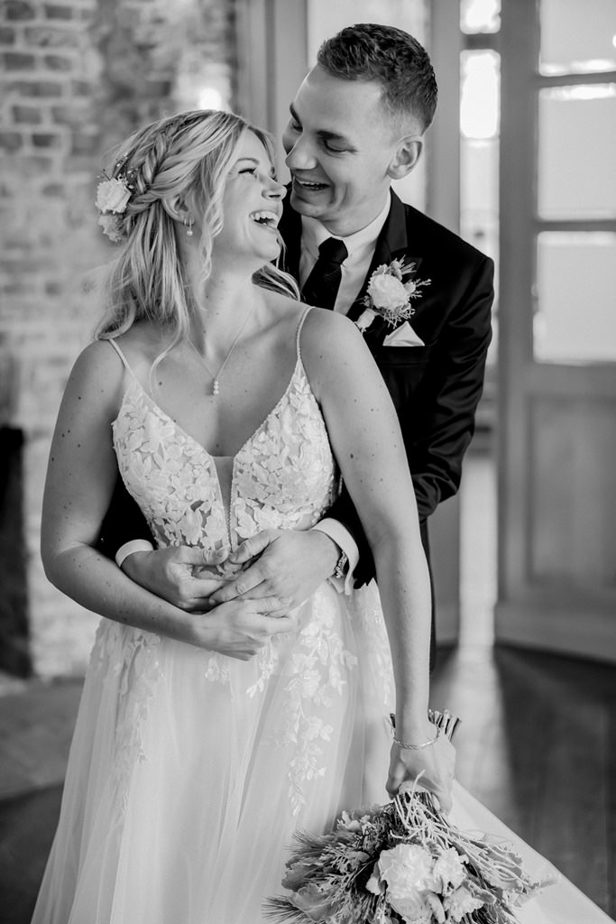 Braut und Bräutigam lachen, während er von hinten ihre Hüfte umfasst | Foto: Hanna Witte
